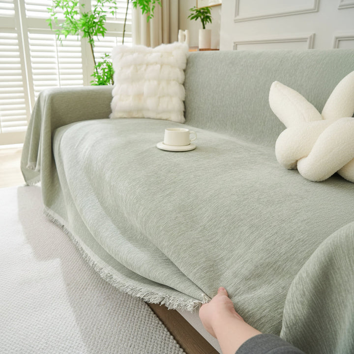 Sage green throw blanket draped over a sofa with a white pillow and cup.