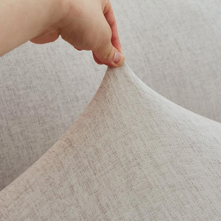 Hand stretching an eggshell colored couch cover with a subtle cross pattern.