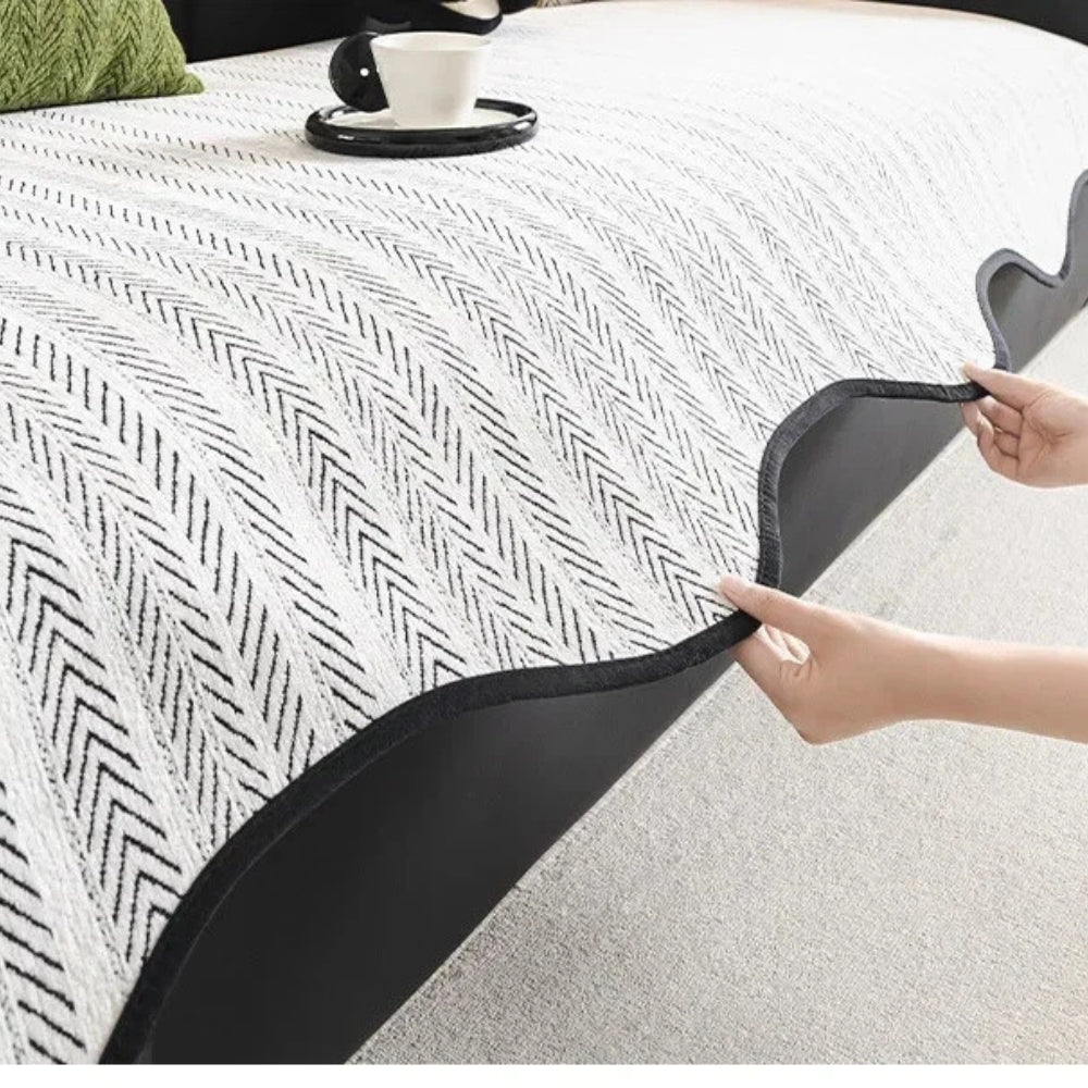 Close-up of a white and black herringbone sofa cover with a scalloped edge being fitted onto a sofa.