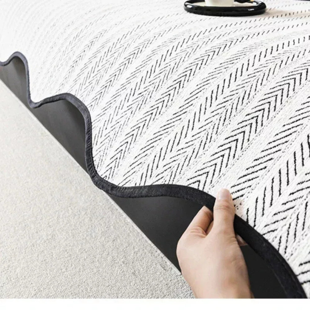 Close-up of a hand lifting the edge of a white herringbone sofa cover, revealing its dark non-slip backing.