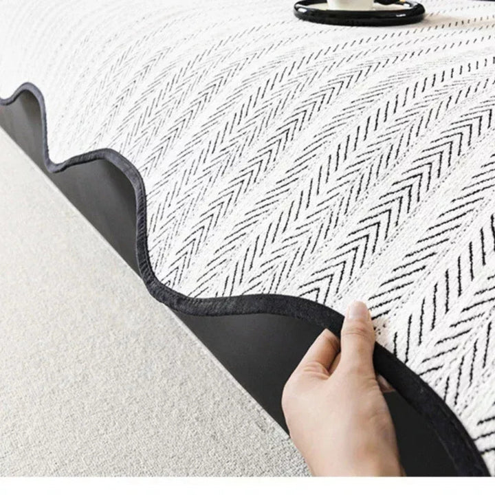 Close-up of a hand lifting the edge of a white herringbone sofa cover, revealing its dark non-slip backing.