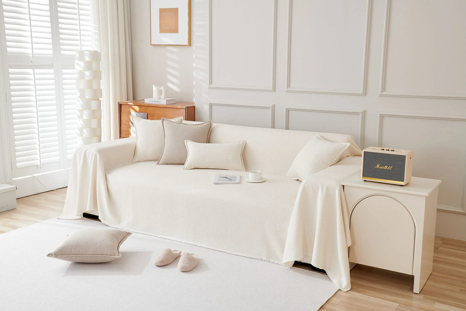Off-white soft throw blanket draped over a sofa with decorative pillows and a small speaker.