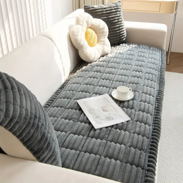 Plush microfiber sofa cover with hand-pleated edges in gray, featuring a white flower pillow and a teacup.