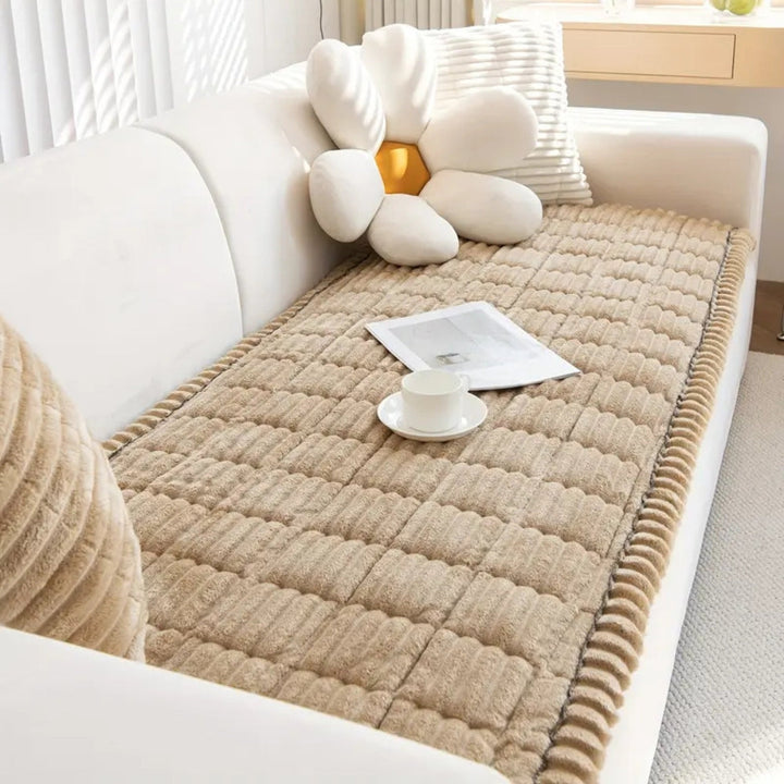 Plush microfiber sofa cover in tan with hand-pleated edges, featuring a white flower pillow and a teacup.