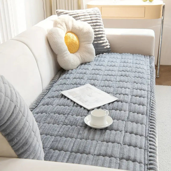 Plush microfiber sofa cover with hand-pleated edges in gray, featuring a flower pillow and a teacup.