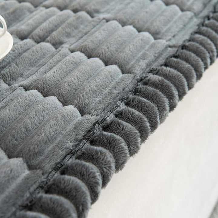 Close-up of a grey plush sofa cover with hand-pleated edges and a textured surface.