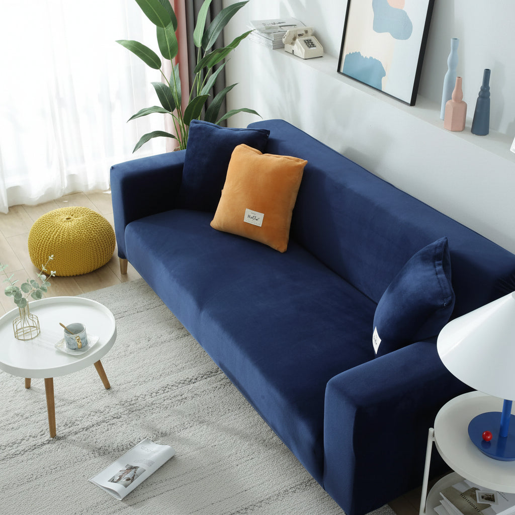 Navy blue velvet couch cover on a sofa with decorative pillows and a yellow ottoman.