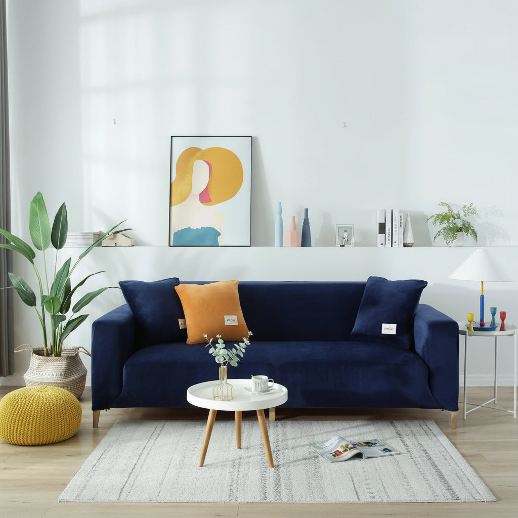 Navy blue velvet couch cover on a sofa with orange and navy pillows, a small white table, and a yellow ottoman.