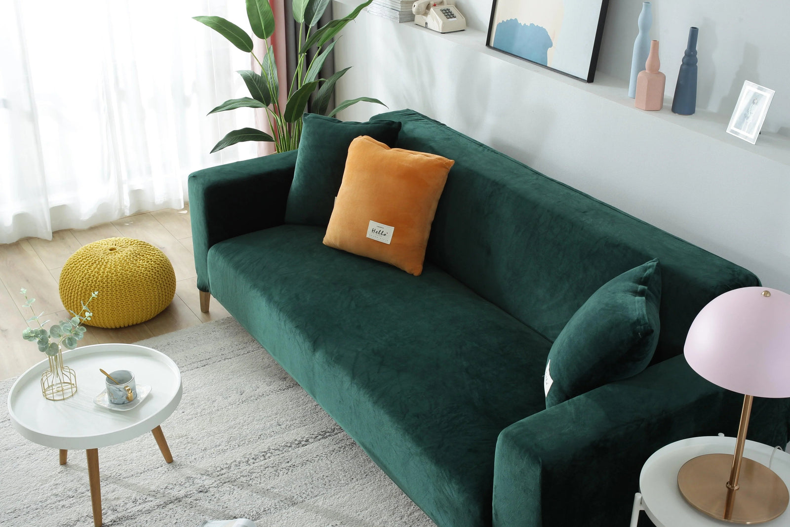 Dark green velvet couch cover with an orange throw pillow and a pink lamp on a side table.