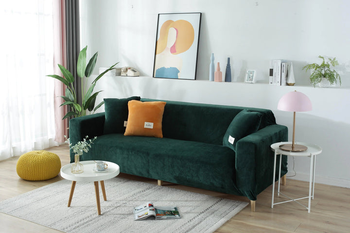 Dark green velvet couch cover with orange and green pillows on a white rug.