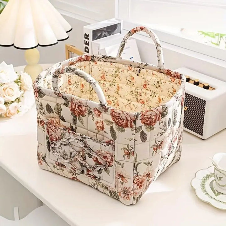 Floral canvas storage basket with handles and ruffled pockets on a white table.