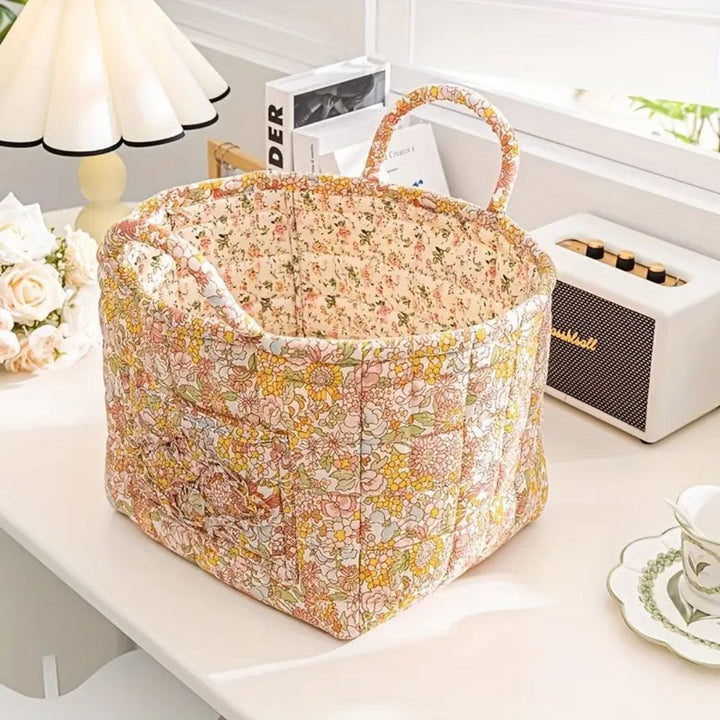 Floral canvas storage basket with handles, open at the top, sitting on a white desk.