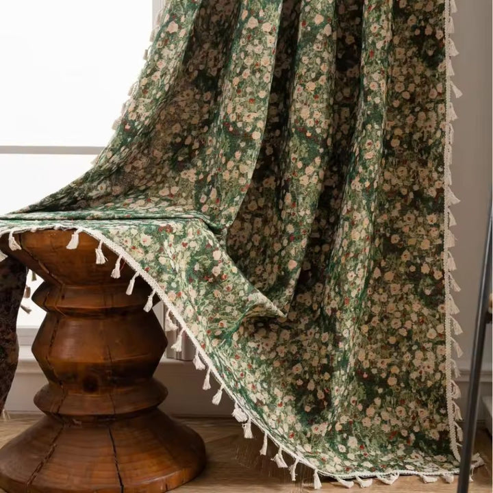Green floral tapestry curtain with white tassels draped over a wooden stool.