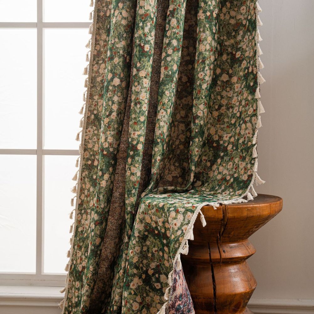Green floral tapestry curtain with tassels draped over a wooden stool.