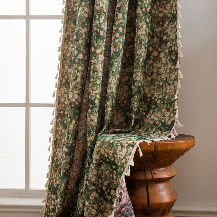 Green floral tapestry curtain with tassels draped over a wooden stool.