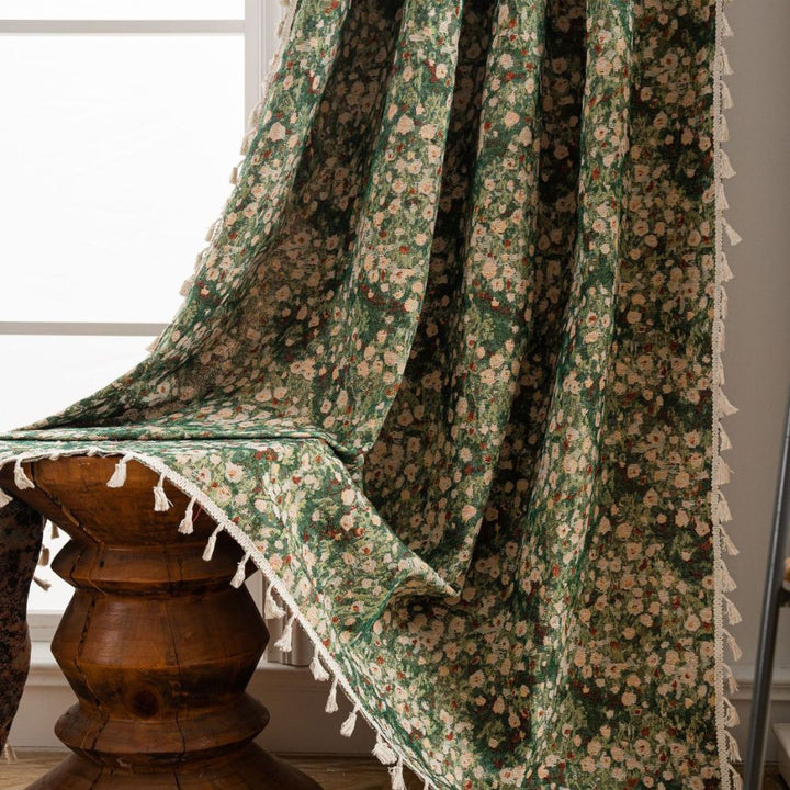 Green floral tapestry curtain with cream tassels draped over a wooden stool.