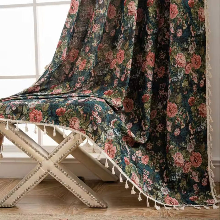 Dark floral tapestry curtain with pink roses and white tassels draped over a bench.