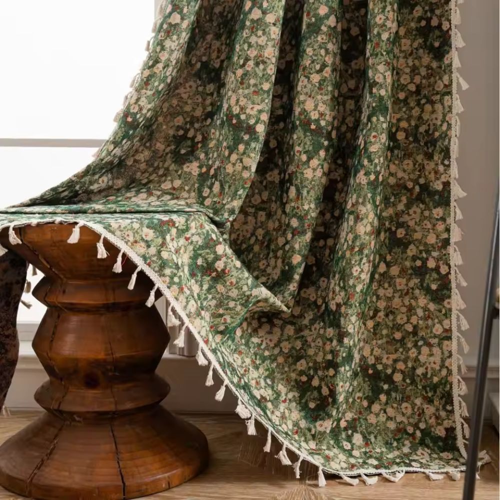 Green floral tapestry curtain with white tassels draped over a wooden stool.