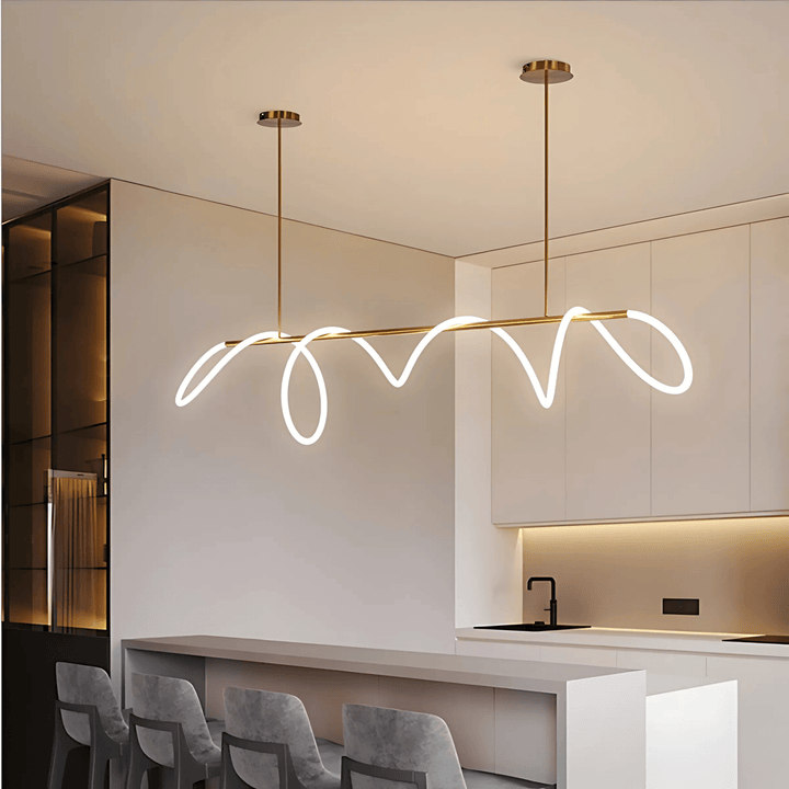 Modern brass chandelier with a wavy white LED light strip, suspended over a kitchen island with bar stools.