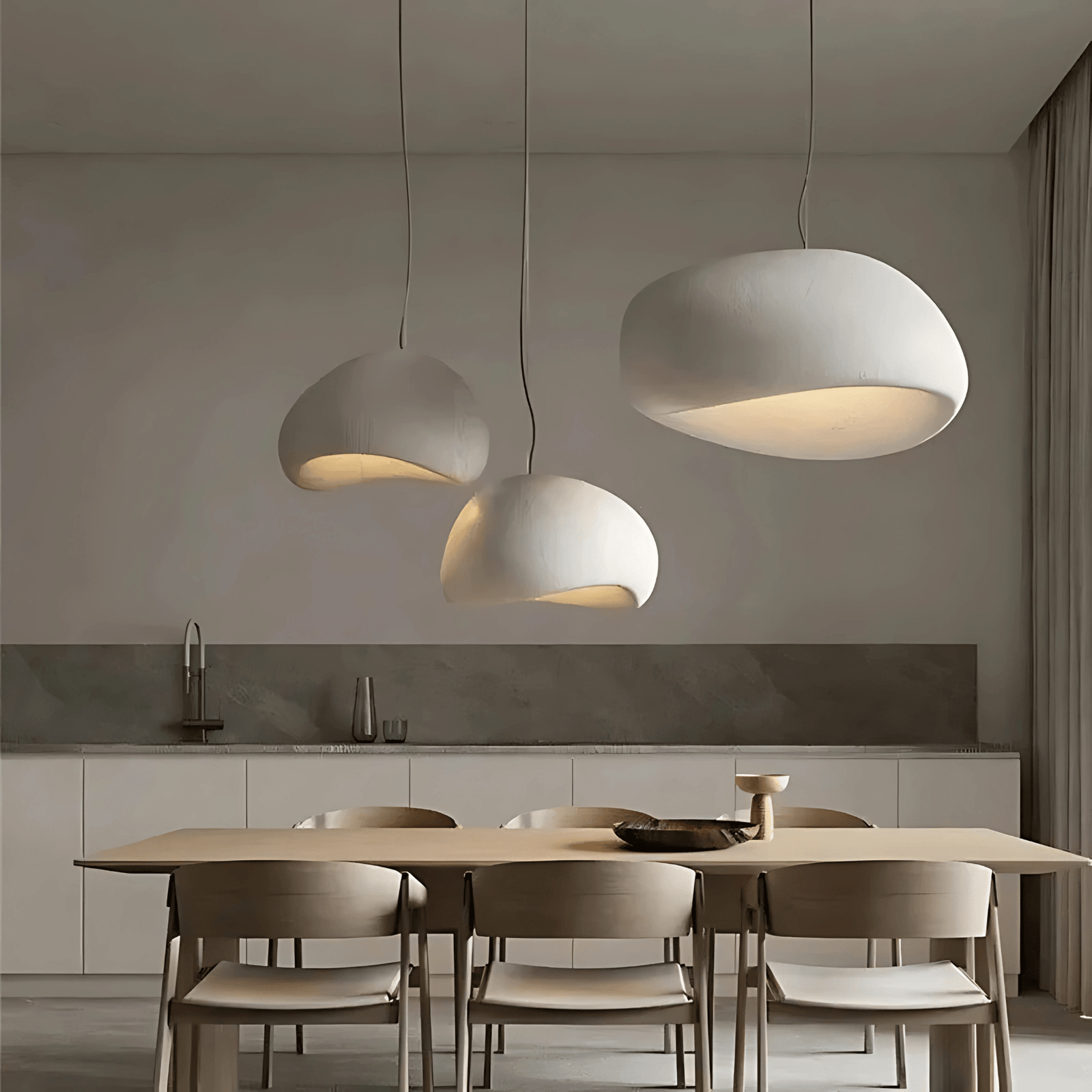 Three off-white Wabi-Sabi pendant lights hanging over a wooden dining table.