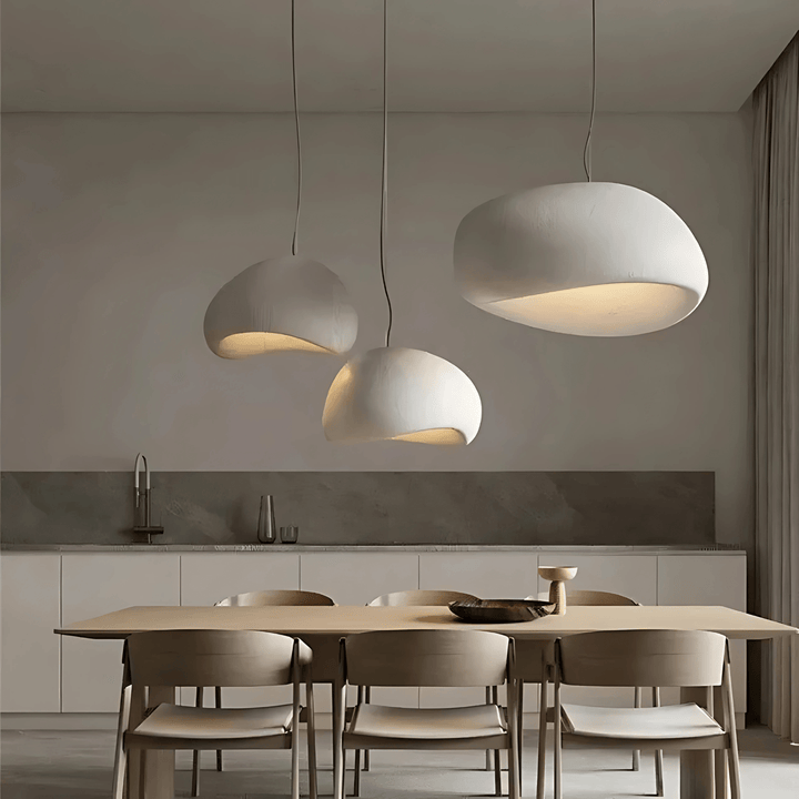 Three off-white Wabi-Sabi pendant lights hanging over a wooden dining table.