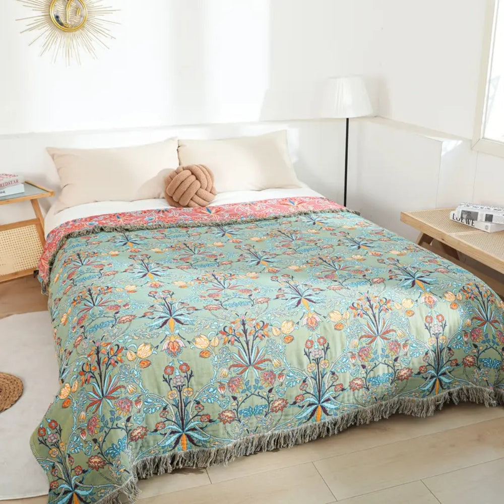 Greenery floral cotton tassel blanket draped on a bed with white pillows and a knot pillow.