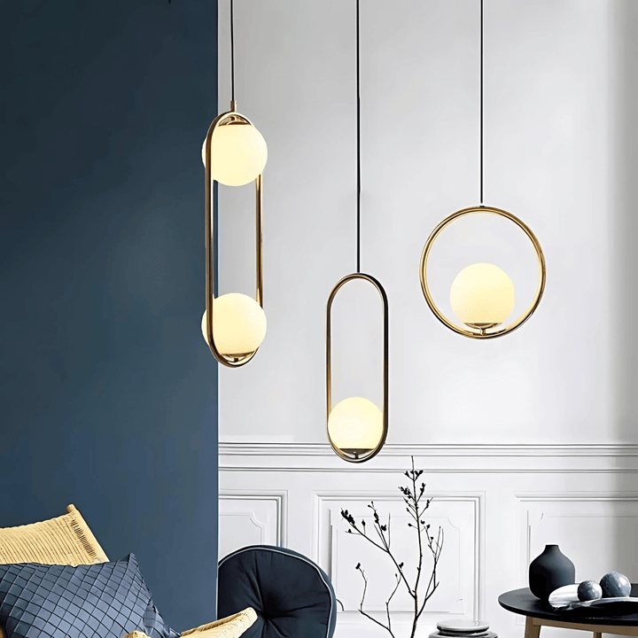 Three minimalist pendant lights with gold frames and frosted glass globes hang against a wall.