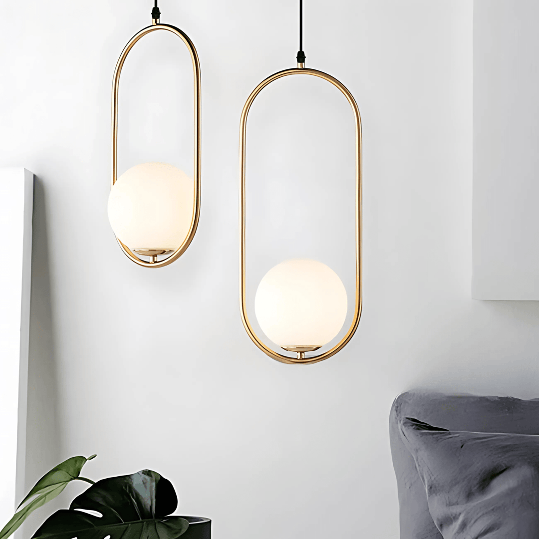 Two gold oval pendant lights with frosted glass globes hanging against a white wall.