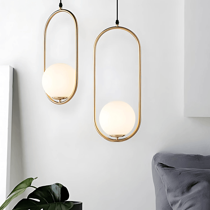 Two gold oval pendant lights with frosted glass globes hanging against a white wall.