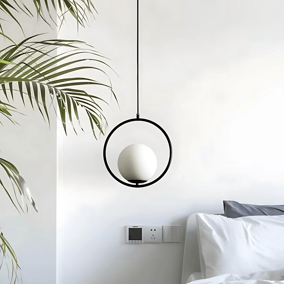 Minimalist black ring pendant light with a frosted glass globe, next to a palm plant.