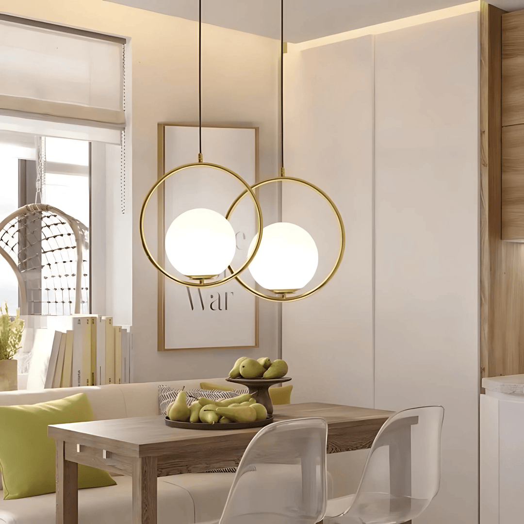 Two gold ring pendant lights with white glass globes hang over a wooden dining table.