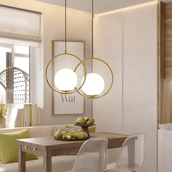 Two gold ring pendant lights with white glass globes hang over a wooden dining table.