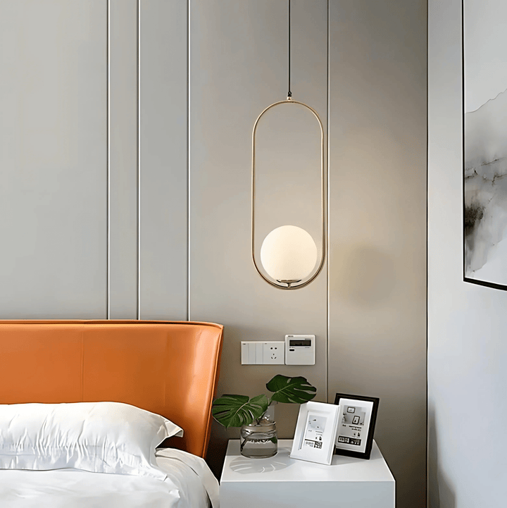 Gold oval frame pendant light with a frosted white globe hangs above a bedside table.