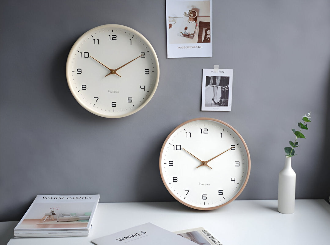 Two Nordic-style wall clocks with white faces, black numerals, and gold hands against a grey wall.