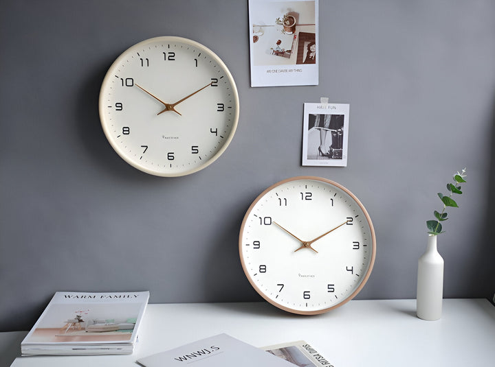 Two Nordic-style wall clocks with white faces, black numerals, and gold hands against a grey wall.