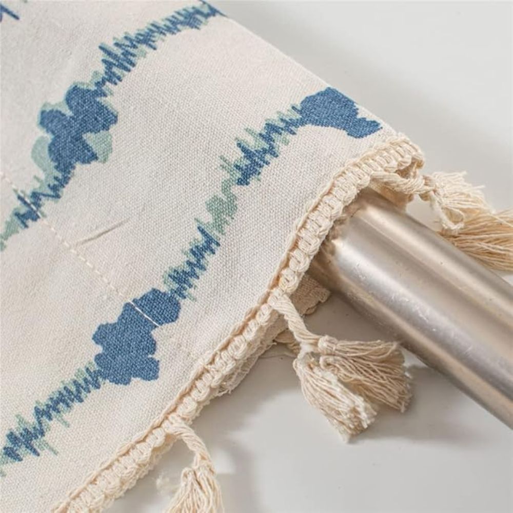 Close-up of a cream-colored cabinet curtain with a blue inkblot pattern and tassel fringe.