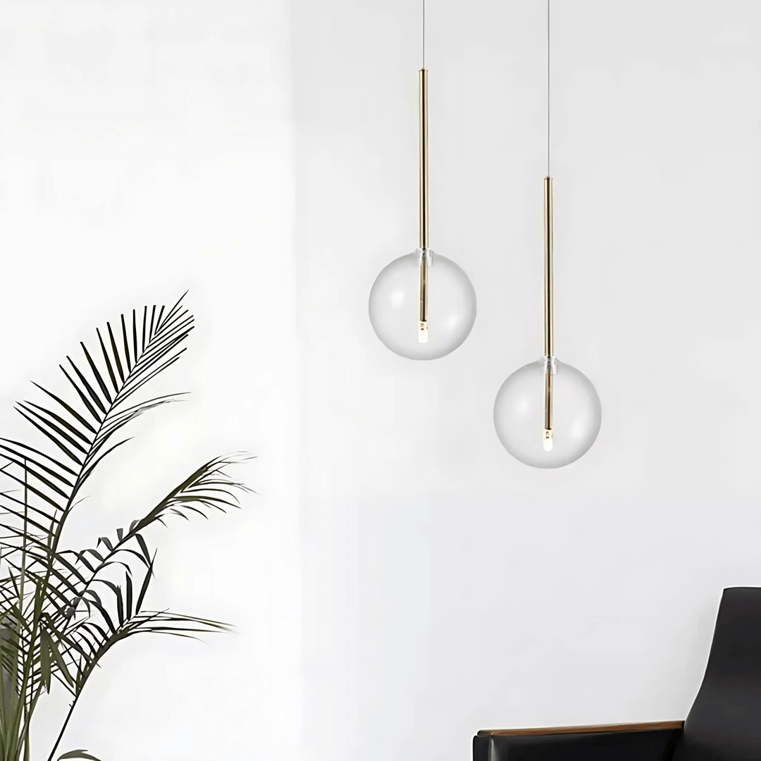 Two modern glass globe pendant lights hanging against a white wall, with a palm frond in the foreground.