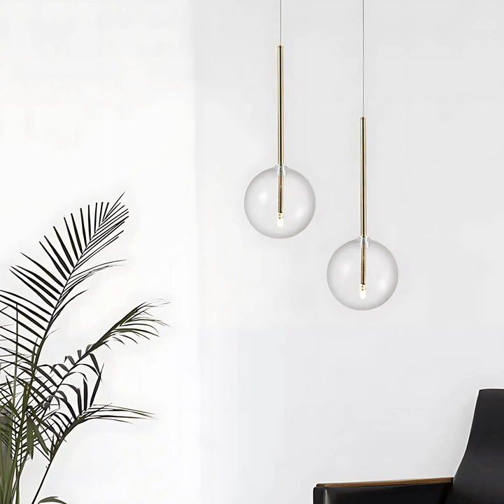 Two modern glass globe pendant lights hanging against a white wall, with a palm frond in the foreground.
