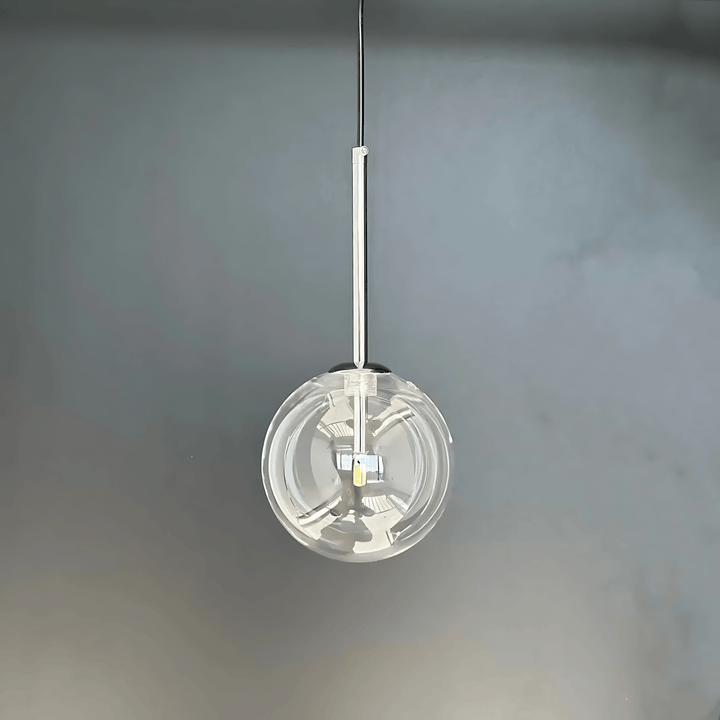 Clear glass globe pendant light with chrome accents hanging from a rod against a gray background.