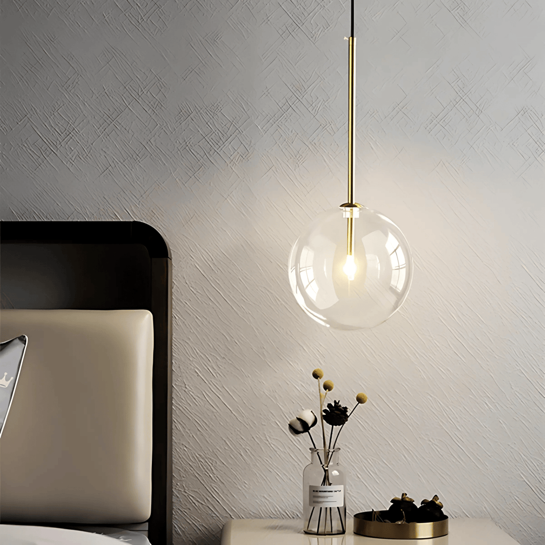 Modern glass pendant light with a gold stem hanging over a nightstand with a vase of flowers.