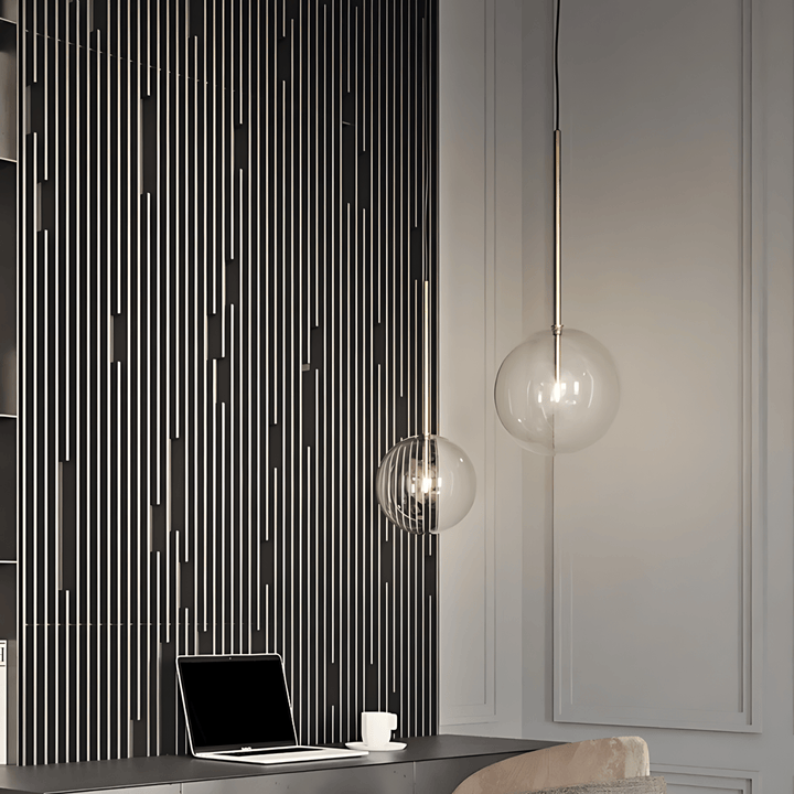 Modern glass pendant light with a sleek metal stem, illuminating a desk area.