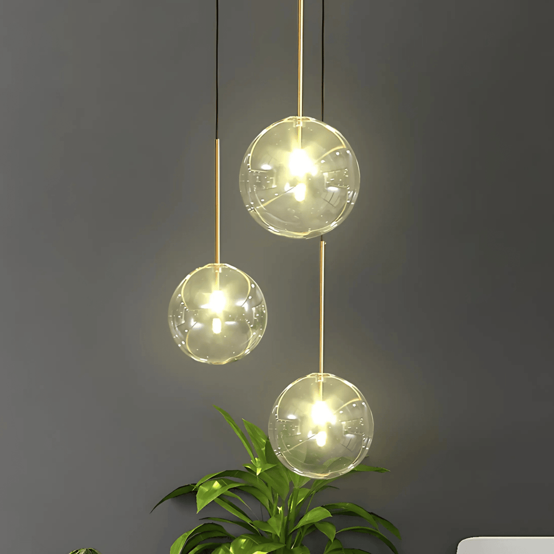 Three clear glass globe pendant lights with gold accents hang against a dark gray wall.