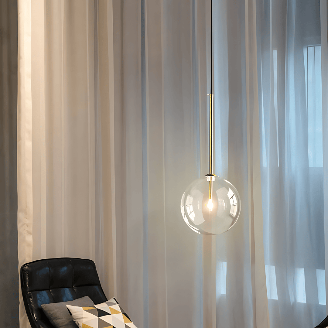 Modern glass globe pendant light with gold accents hanging over a black leather chair.
