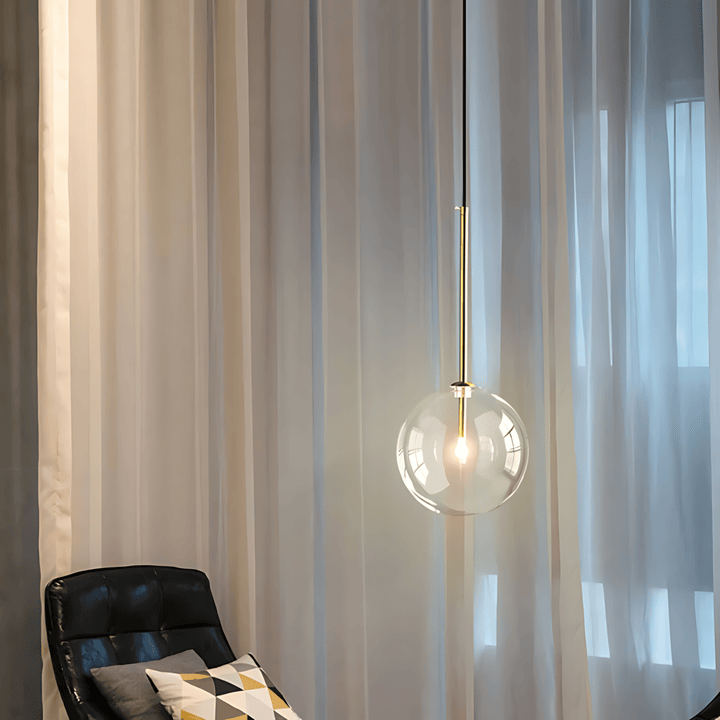 Modern glass globe pendant light with gold accents hanging over a black leather chair.