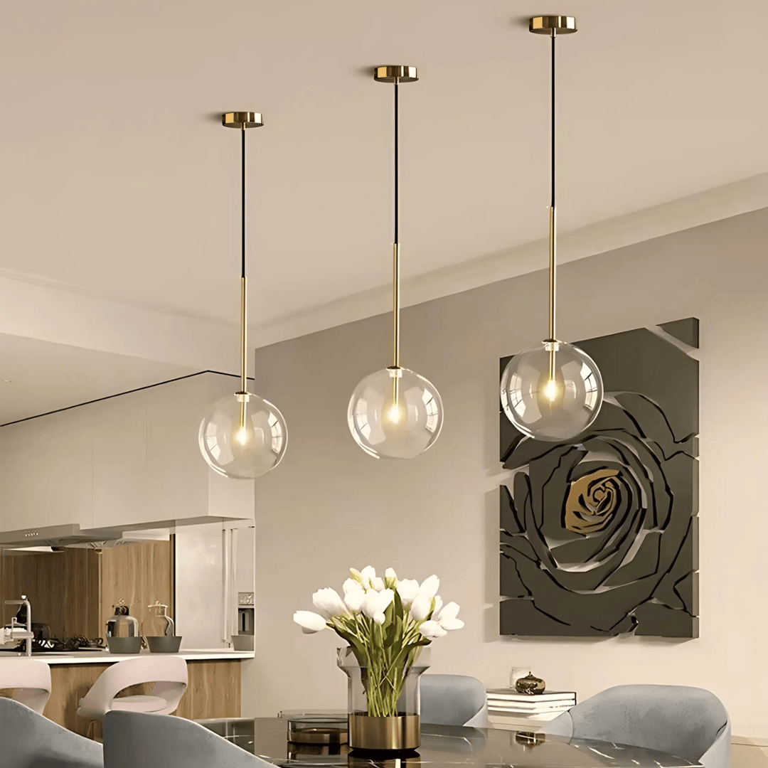 Three modern glass globe pendant lights with gold accents hang over a dining table.