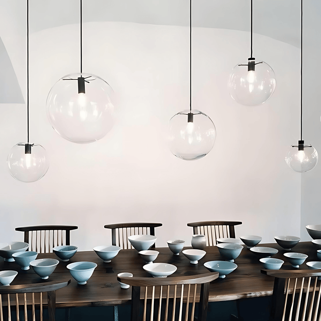 Modern glass globe pendant light hanging over a wooden table with bowls.
