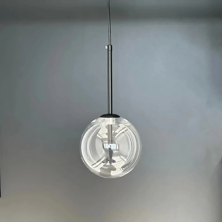 Modern glass pendant light with a clear globe and metal stem against a gray background.
