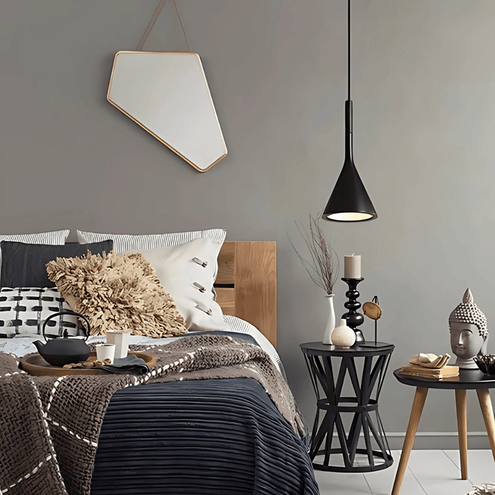 Black cone pendant light hanging over a bedside table with decor.