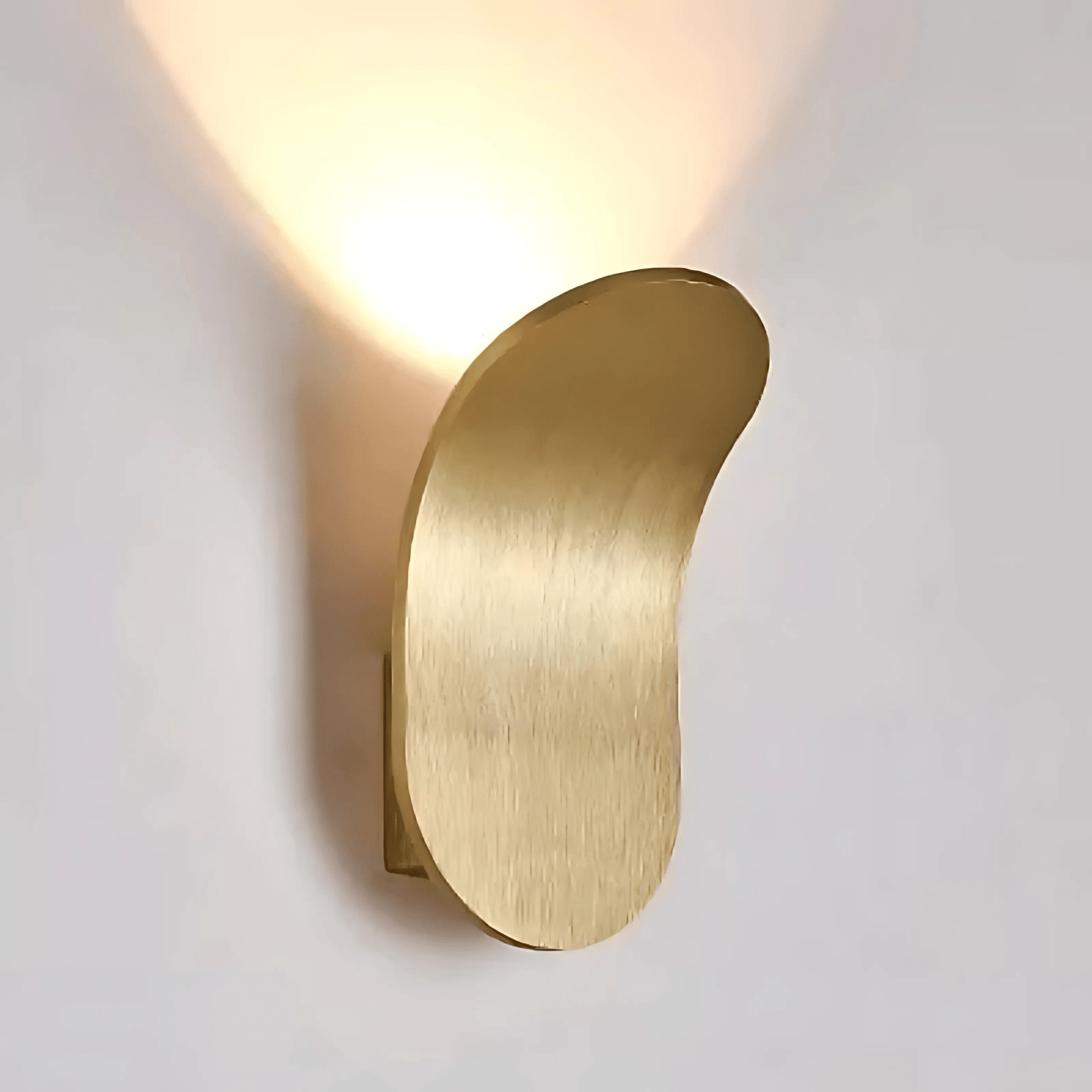 Brushed brass metal wall sconce with a curved, organic shape, casting a warm light upwards.
