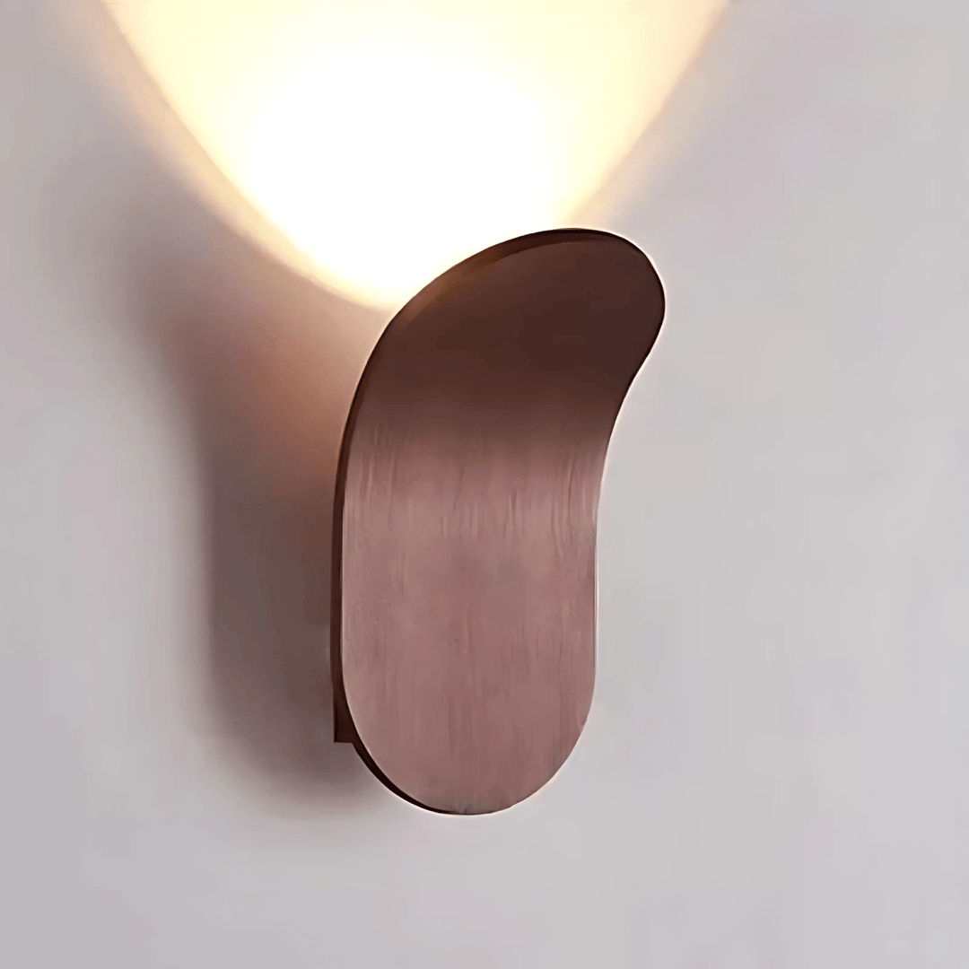 Modern metal wall sconce with a curved, oval shape in a brushed copper finish, casting a warm light upwards.